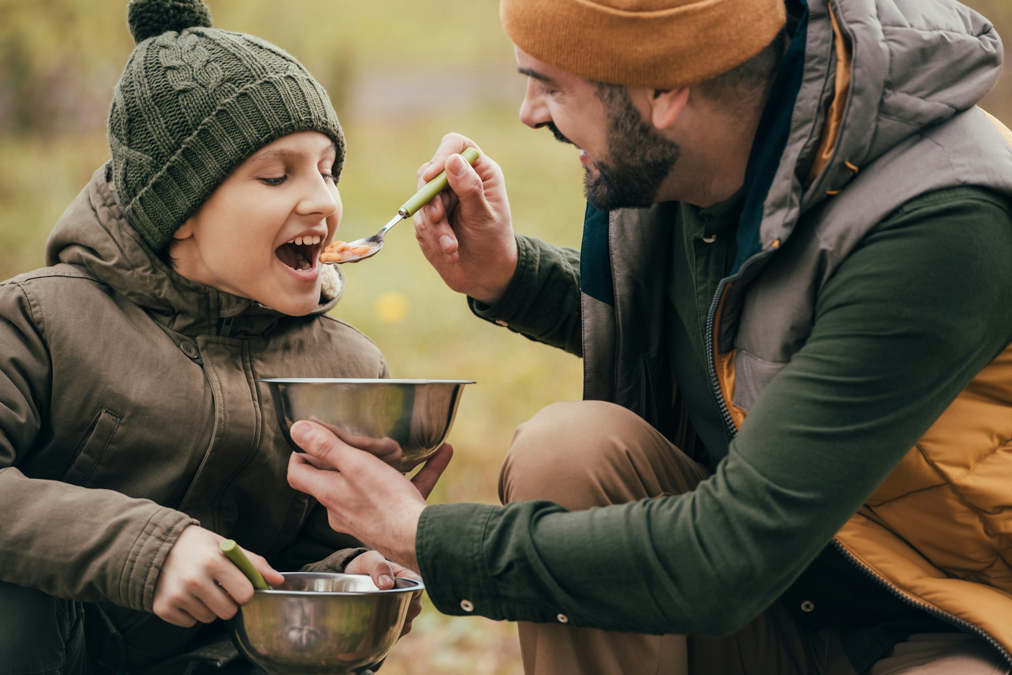Father giving spoon with beans to son on a nature