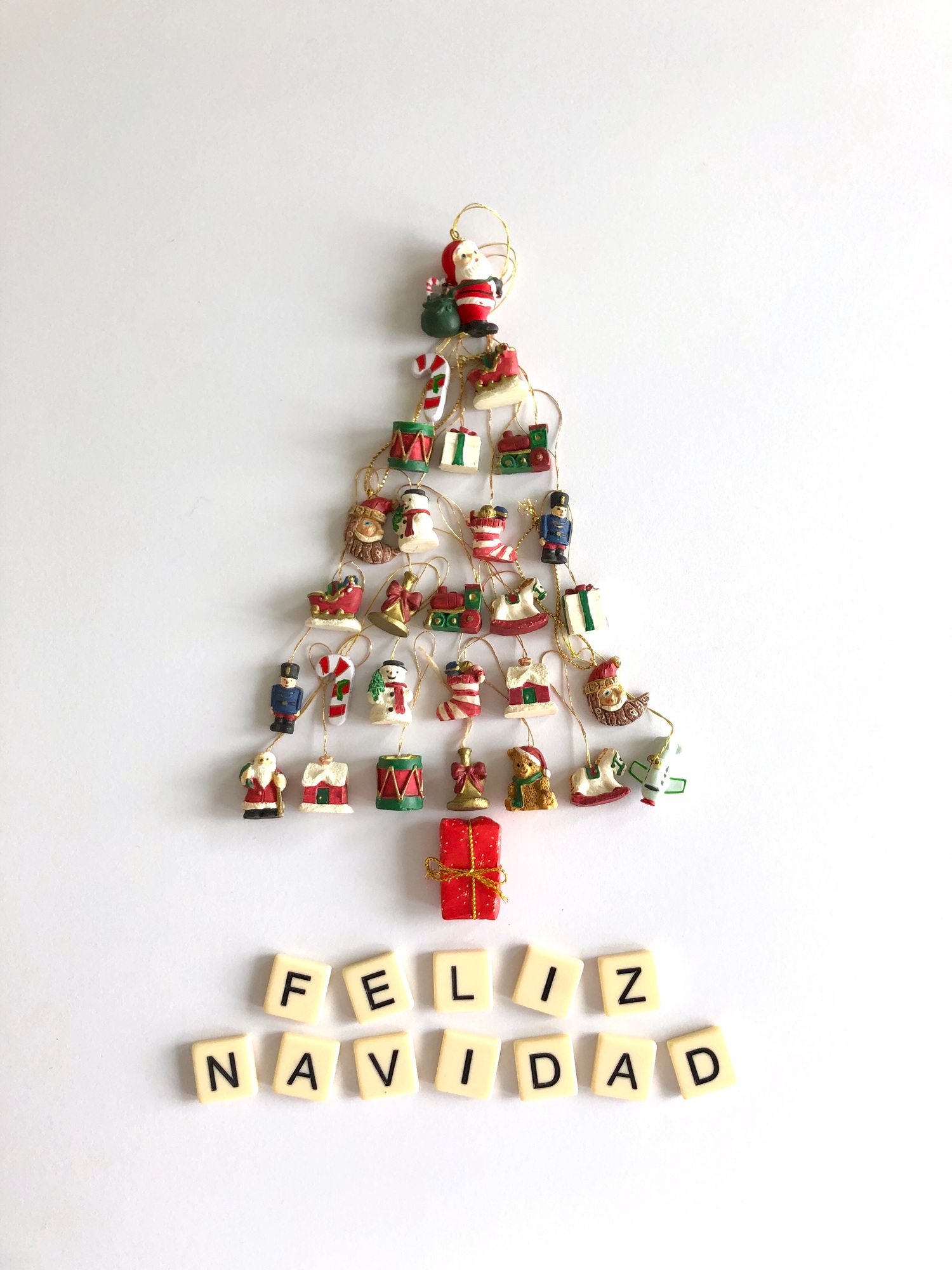 Christmas tree flat lay made with tiny ornaments & Merry Christmas written in Spanish Feliz Navidad